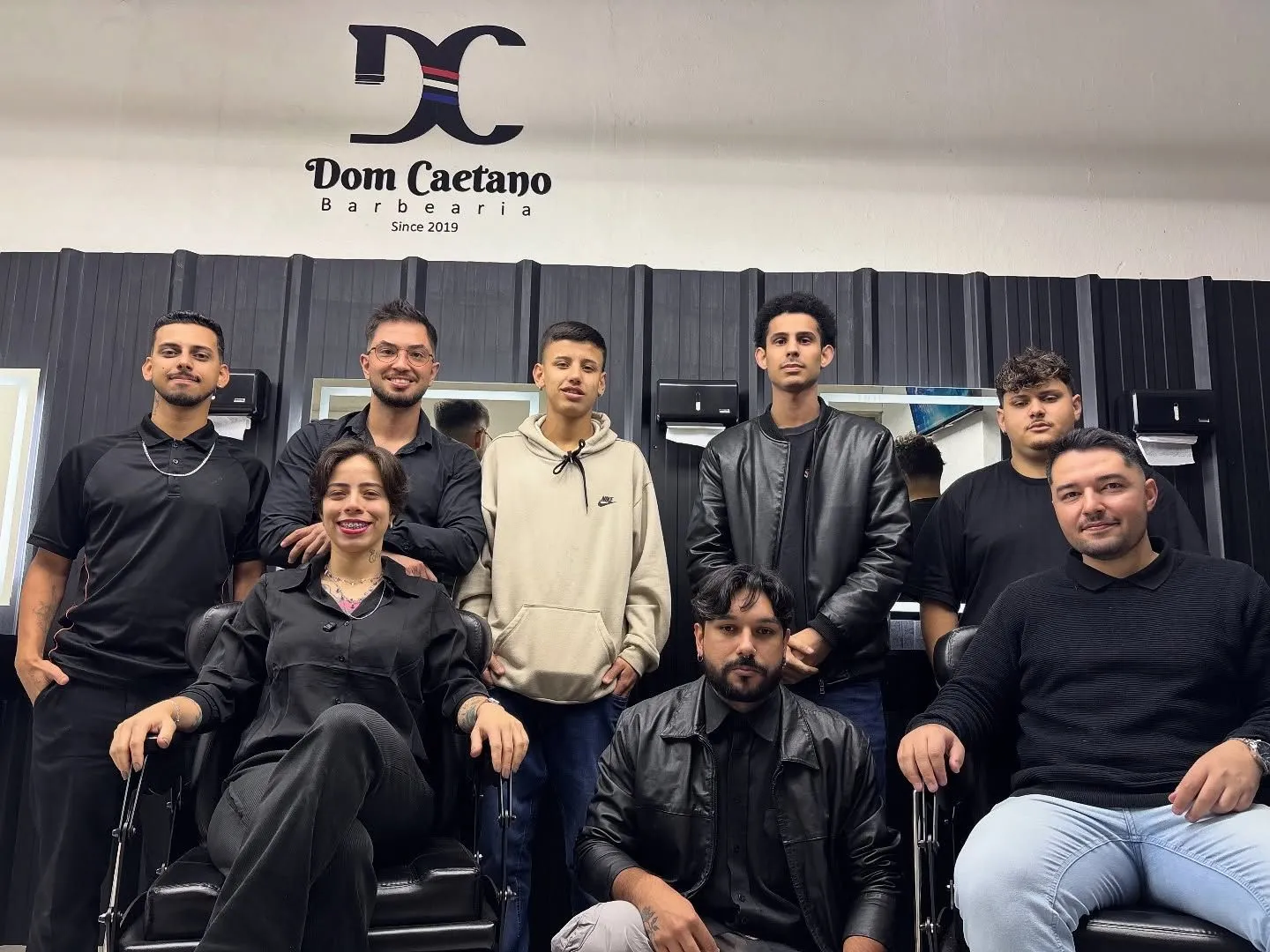 A equipe da Dom Caetano reunida no salão, em frente ao logo pintado na parede.